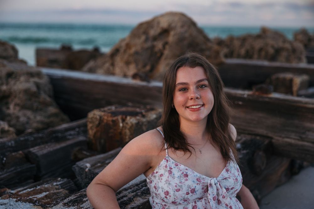 Standing among rocky coastal formations wearing a summery floral dress with ocean views.