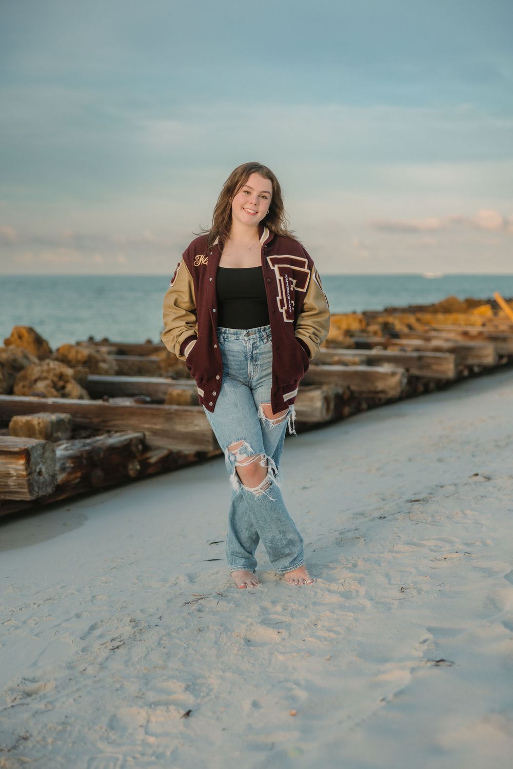 Casual beach portrait on wooden jetty with ocean waves and cloudy sky in background.