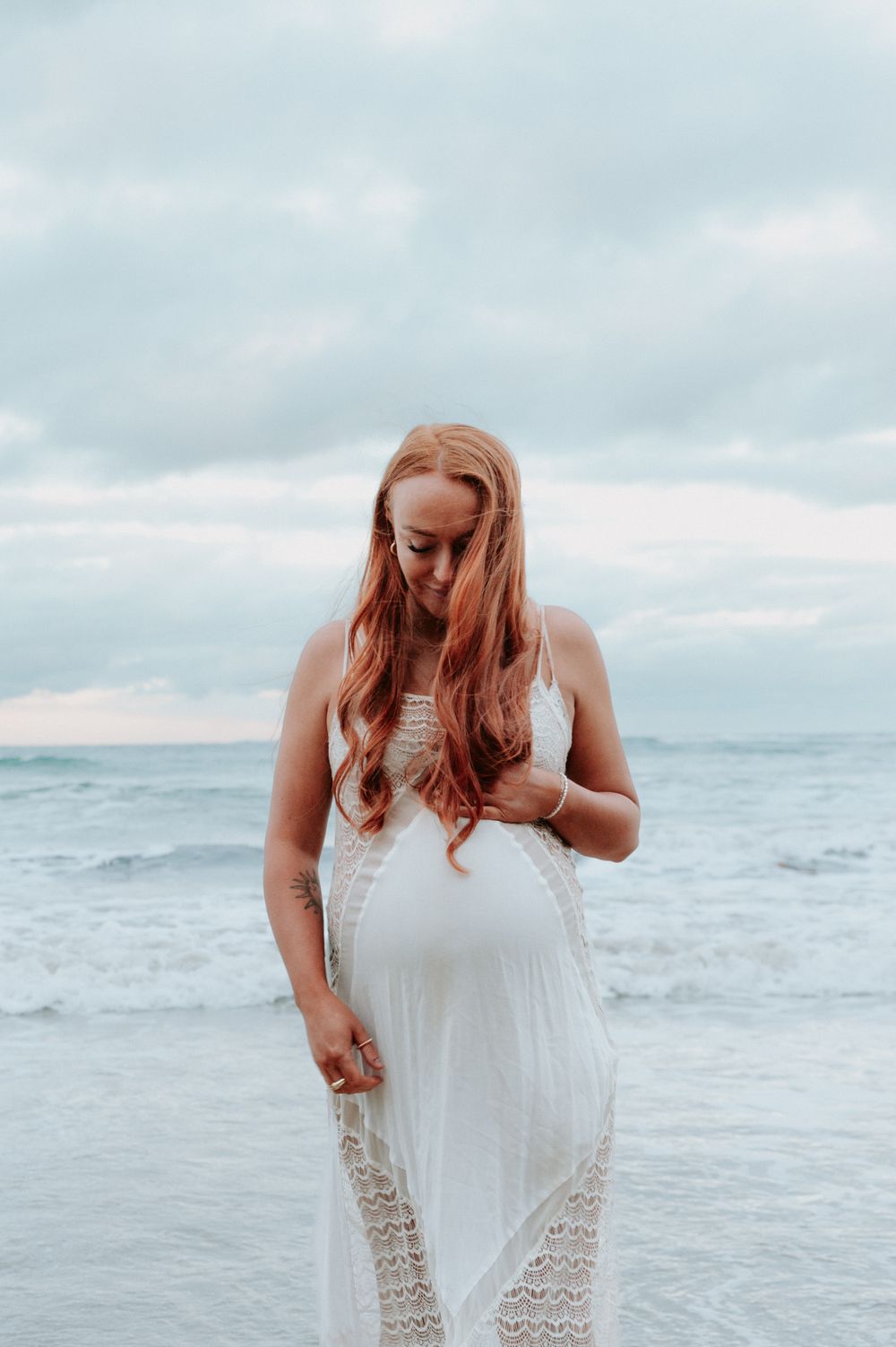 Woman in flowing white dress cradles baby bump against ocean backdrop.
Altona Family Photographer Melbourne