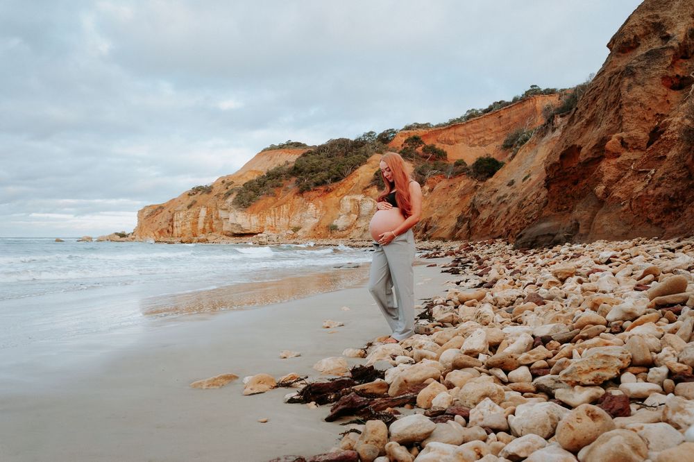 Pregnant woman walks along rocky beach with dramatic coastal cliffs in soft overcast lighting.
Altona Family Photographer Melbourne