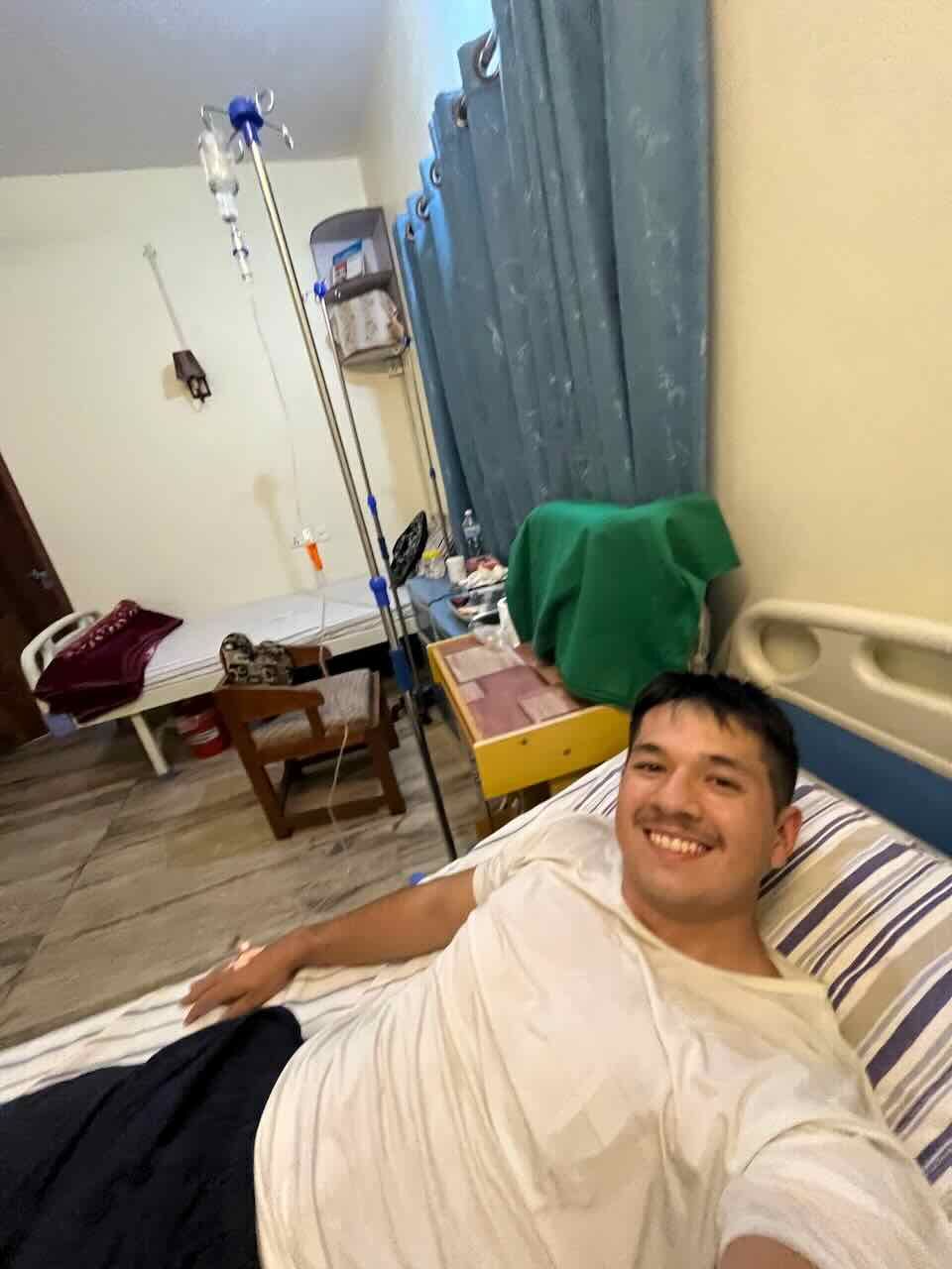 Patient resting in hospital bed with medical equipment visible in background.