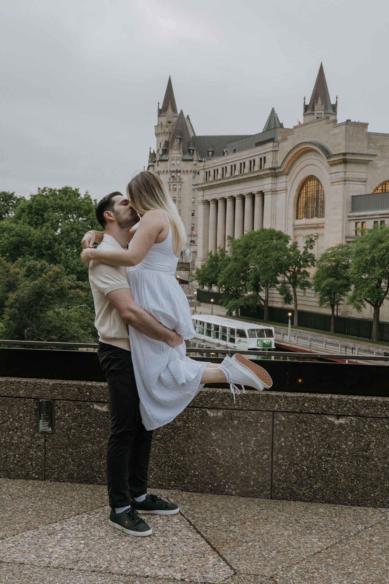 Romantic embrace at the edge of a historic stone building with gothic architecture and towers in Ottawa, Canada.