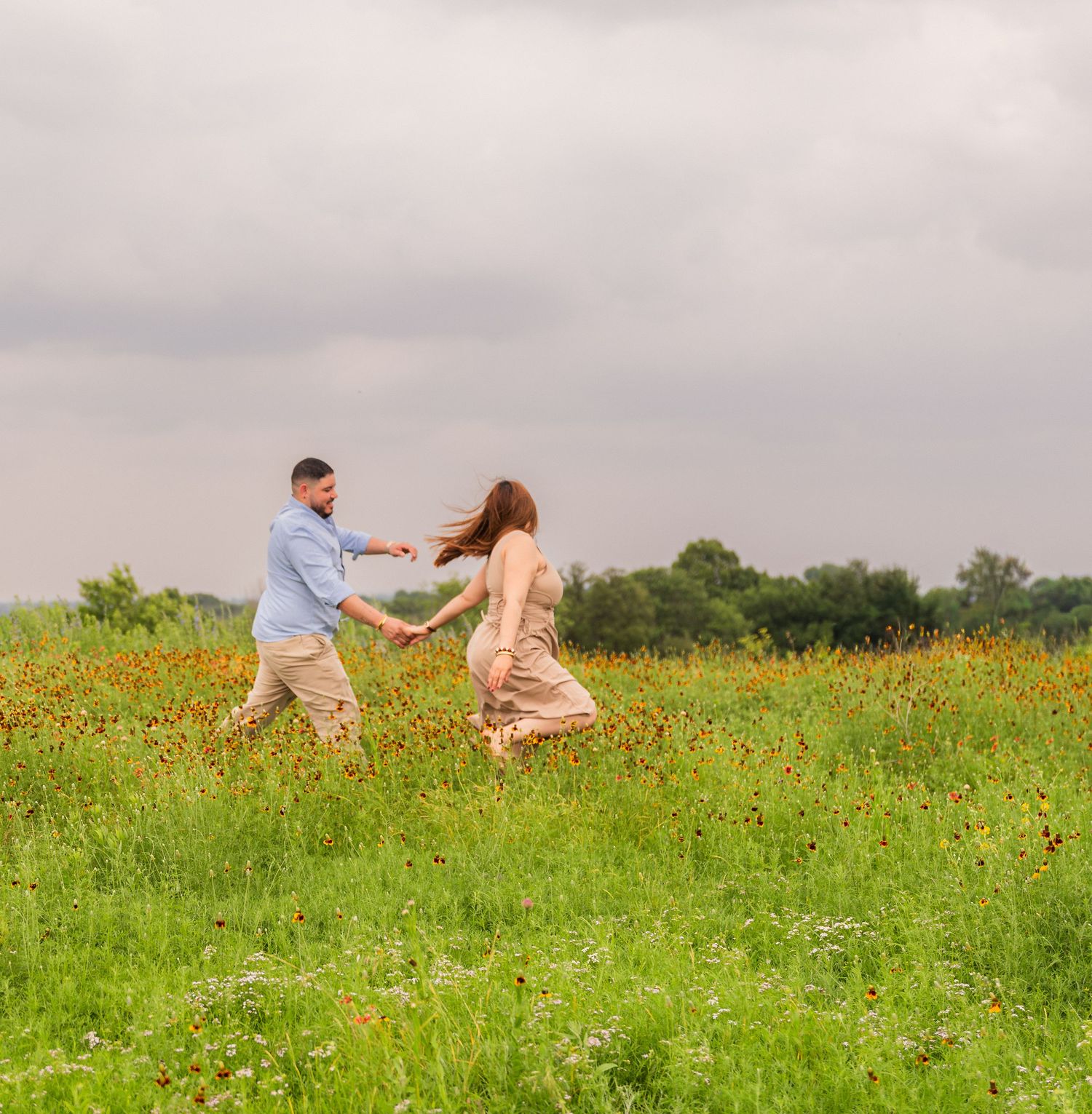 Two people embrace while sitting in a field of tall grass and red wildflowers during a sunny day. Wildflowers in Flower Mound Texas