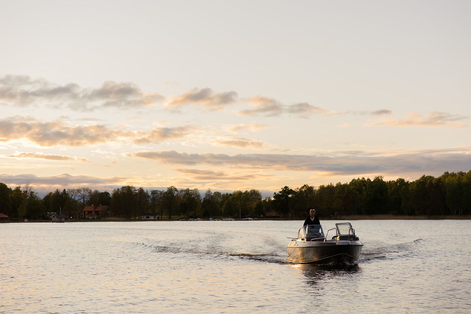 Scenic lake view with boats on calm water at sunset as golden clouds reflect off the water's surface.