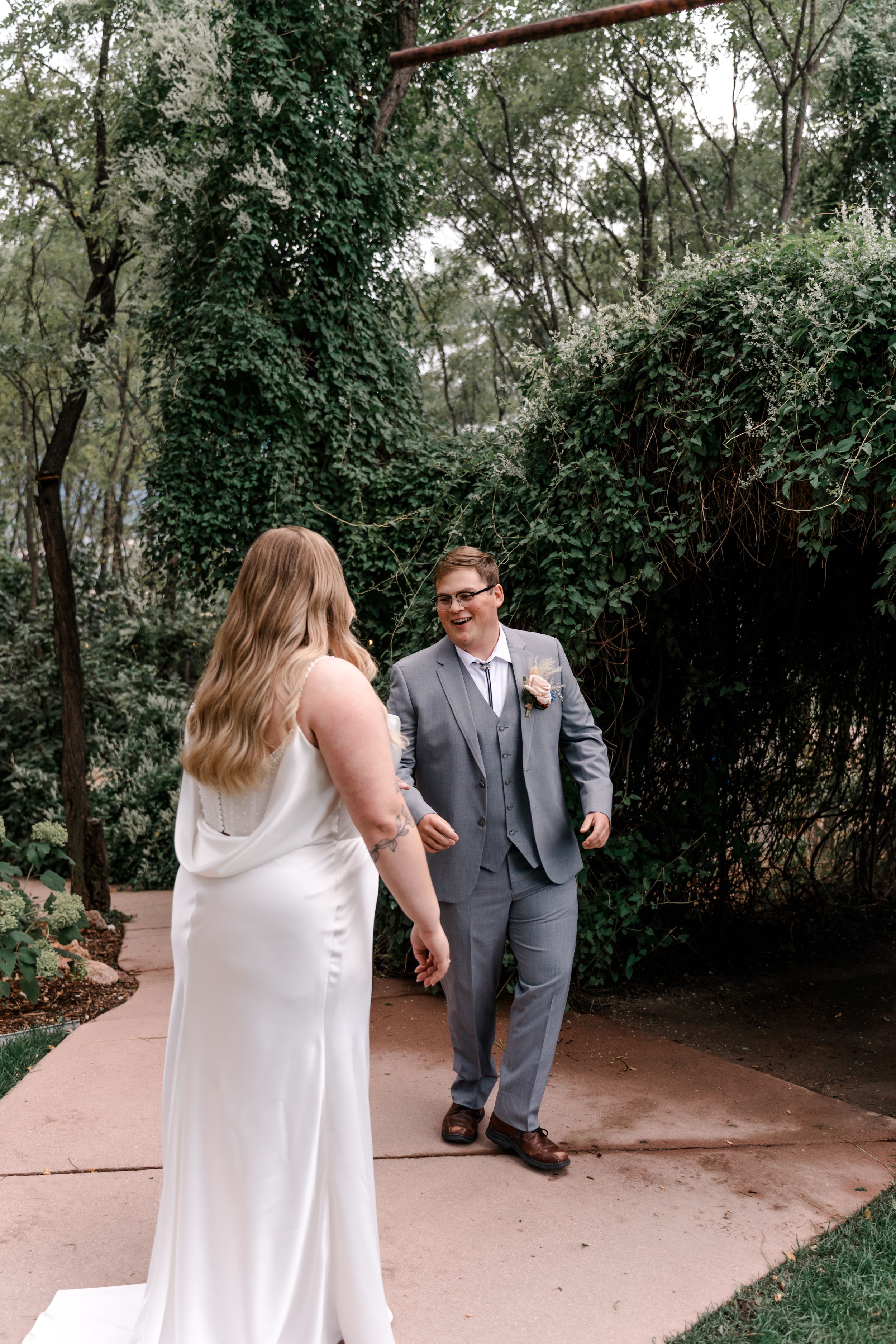 A couple shares a romantic moment on a garden path surrounded by lush greenery and trees.