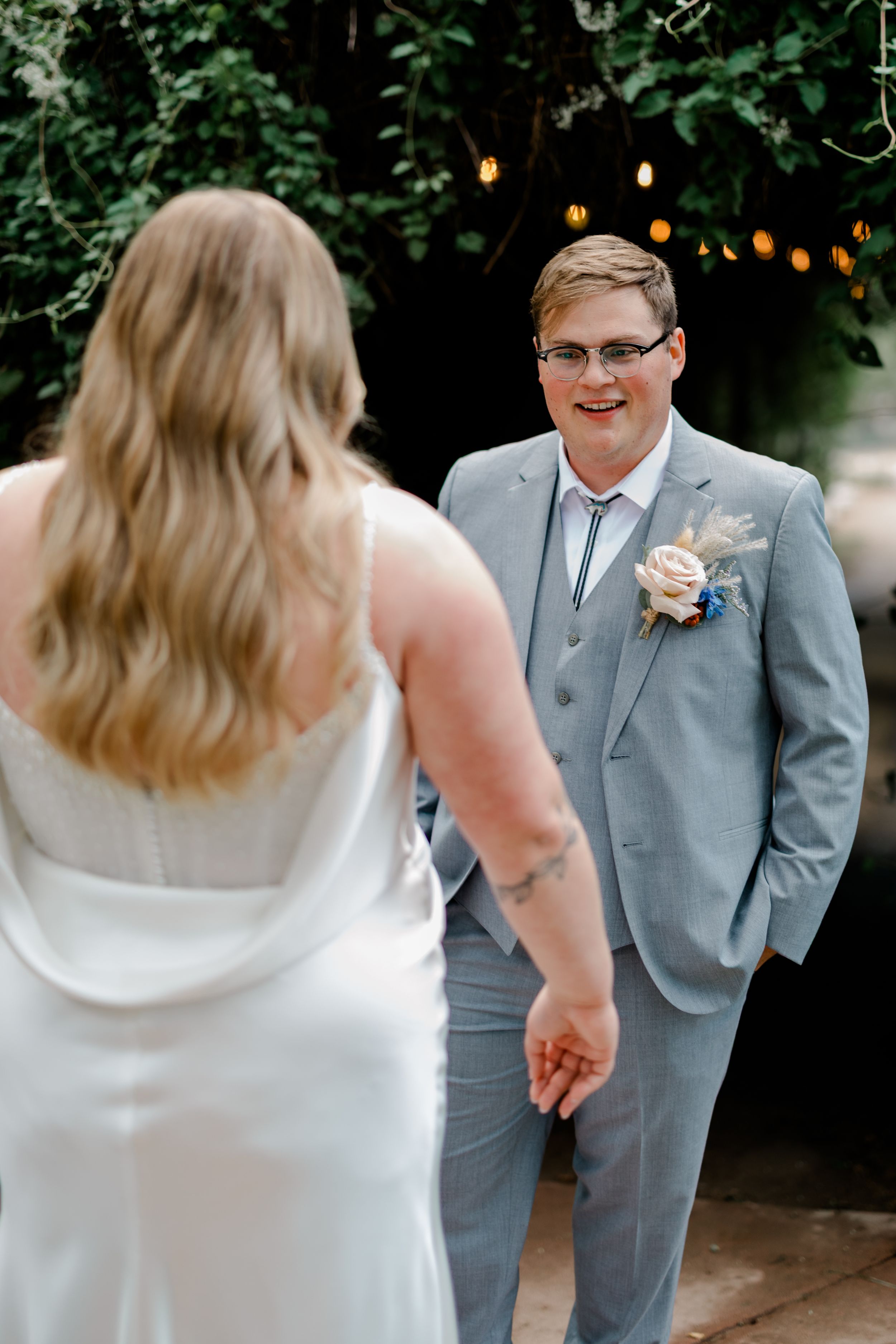A couple shares a tender moment during their wedding first look in a garden setting with string lights overhead.
