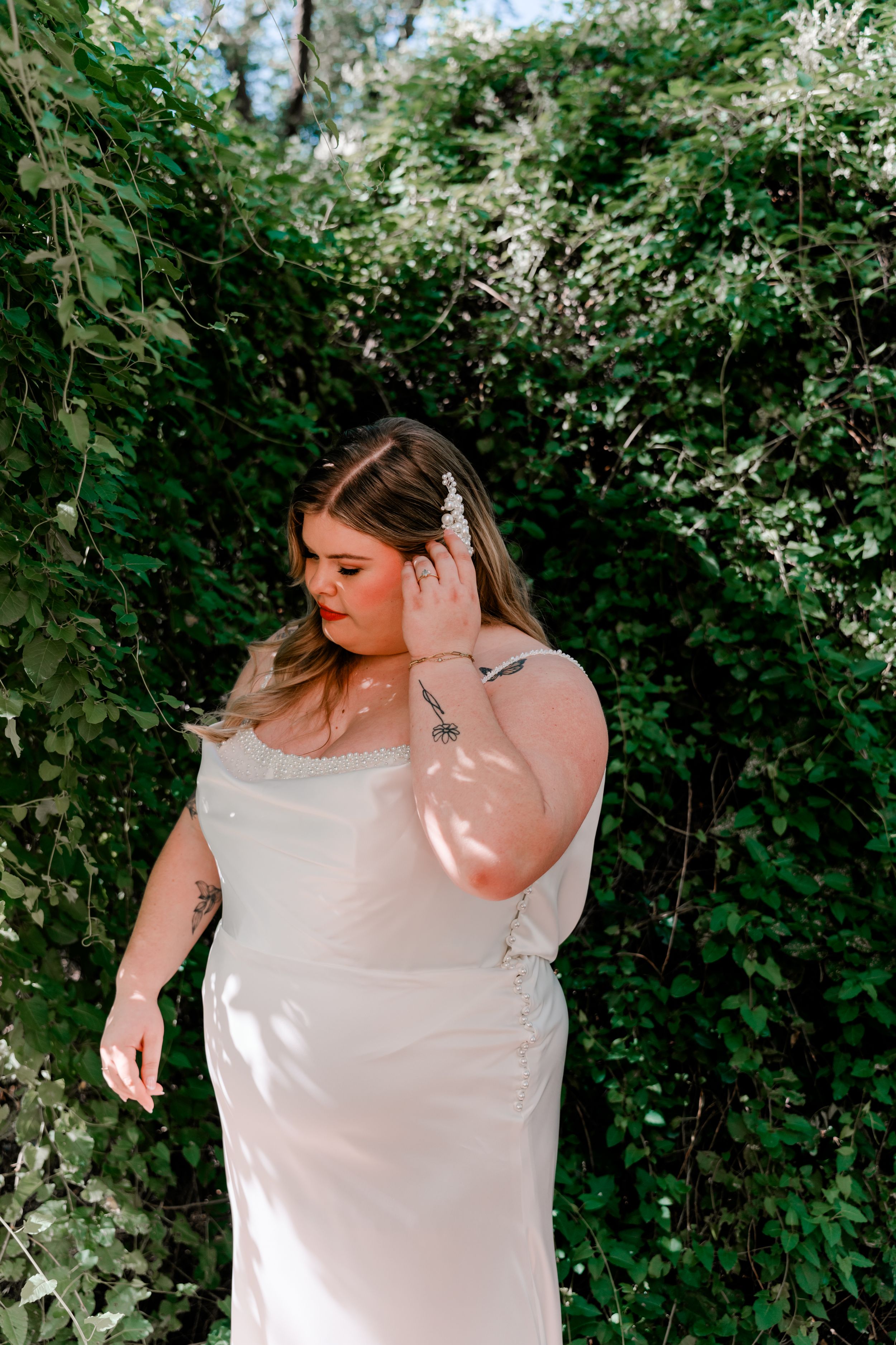 A wedding dress detail shot against lush green foliage and white flowers in a garden setting.