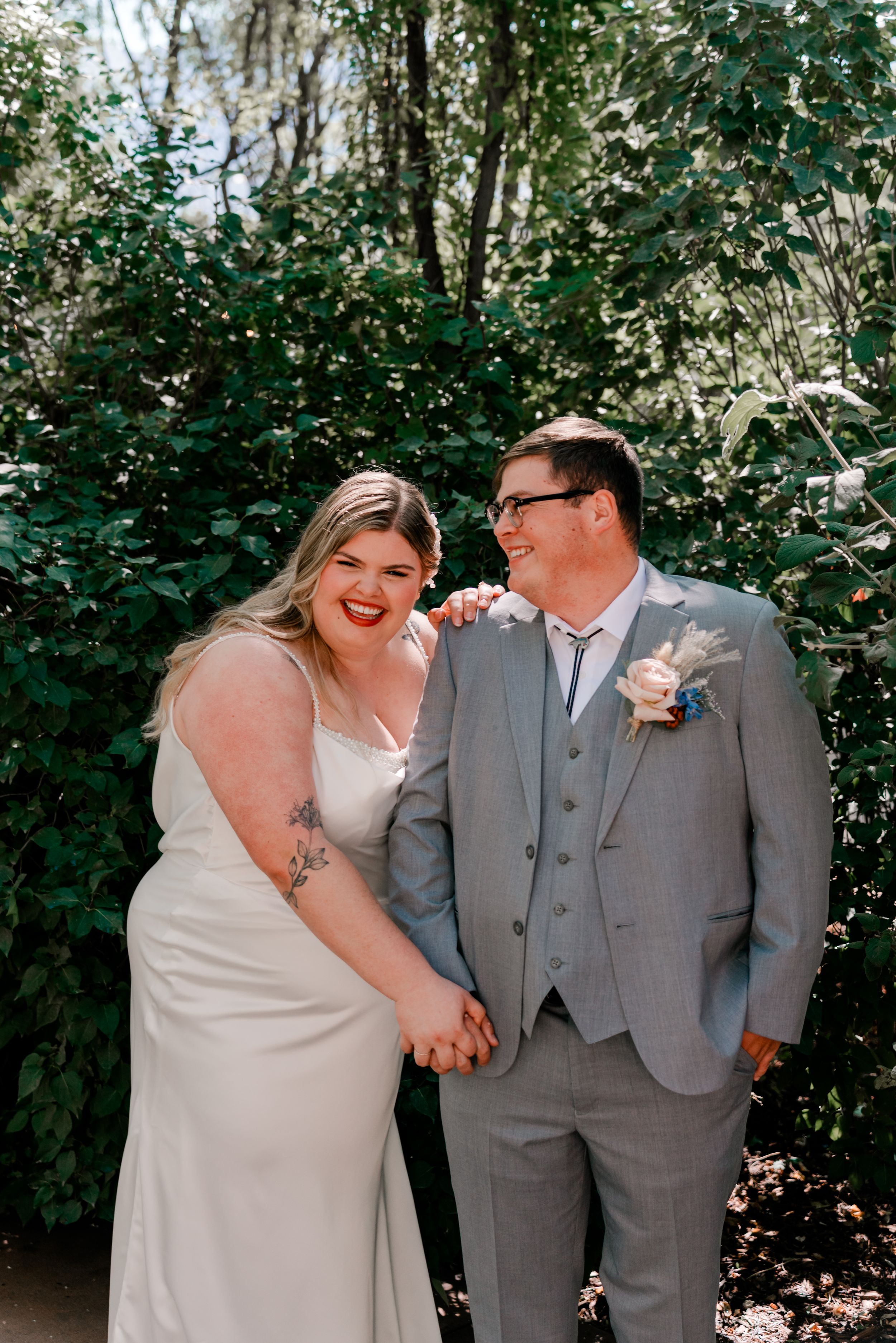 Wedding couple shares joyful laughter together in an outdoor garden setting.