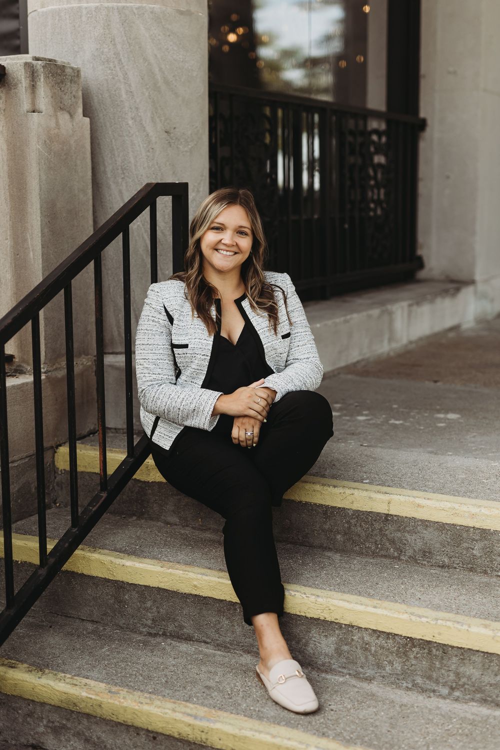 Professional seated on concrete steps wearing a black and white tweed blazer and black pants.