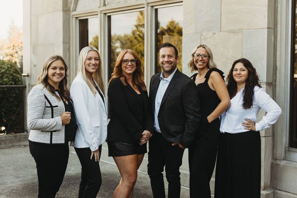 Professional team in black and white business attire poses together for group photos in an outdoor setting.