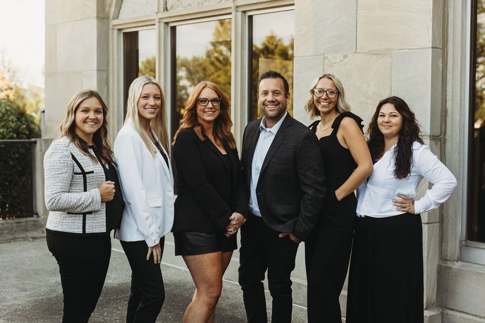 A group of professionals in black and white business attire pose together outdoors for a formal photo.