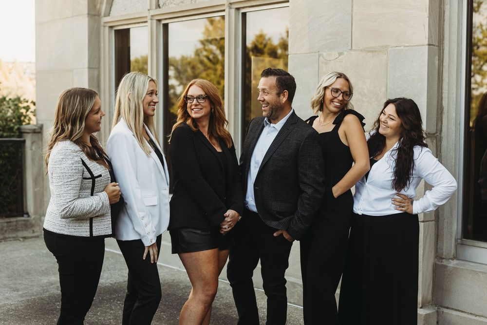 A group of people in black and white business attire gather and socialize in an outdoor hallway.