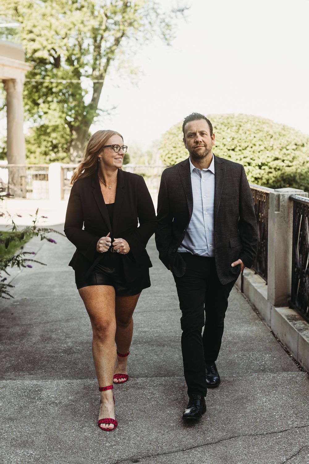 Professional couple walking together outdoors, wearing business attire with her in red heels and him in a suit.