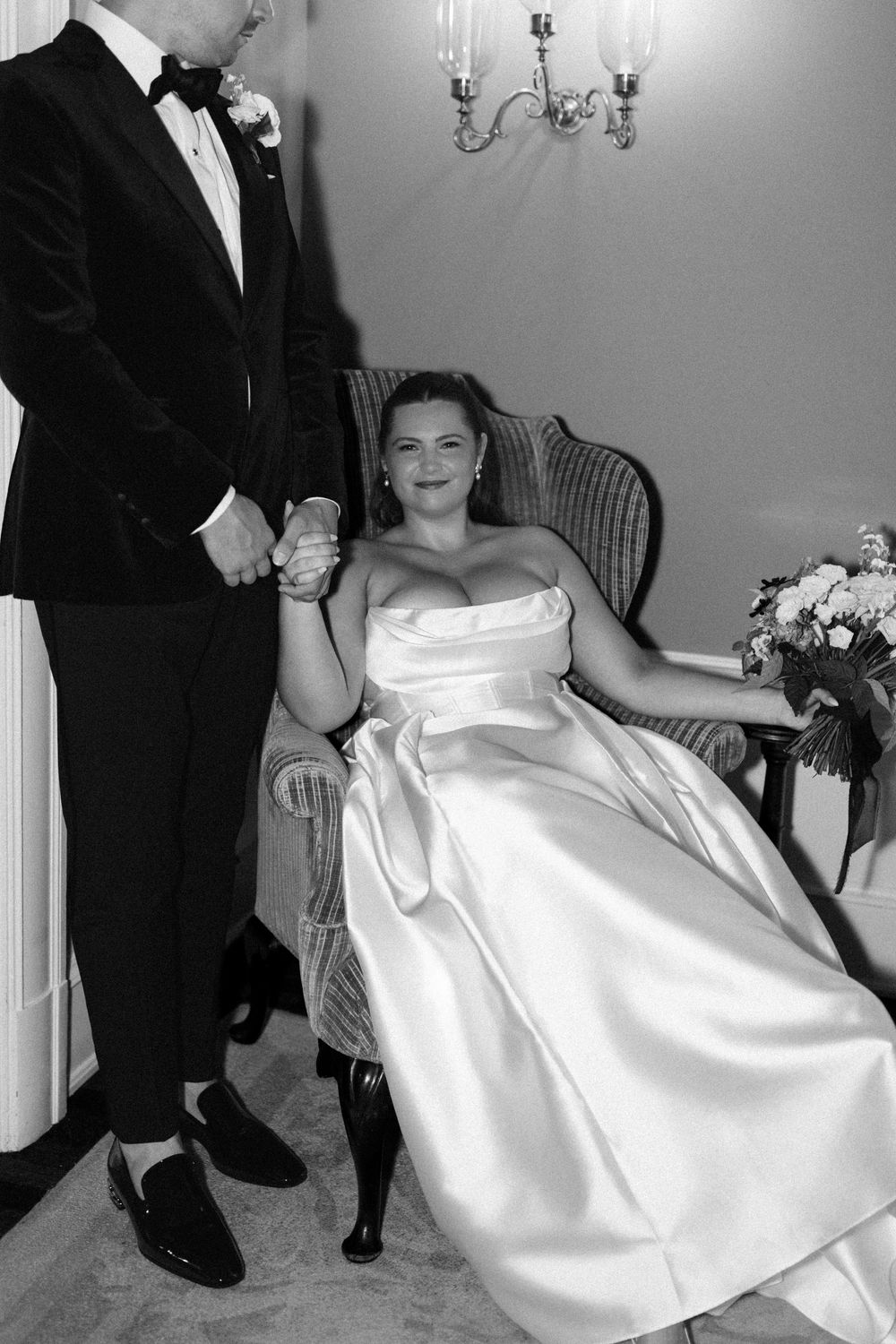 Black and white portrait of a couple in formal wedding attire seated in an elegant setting.