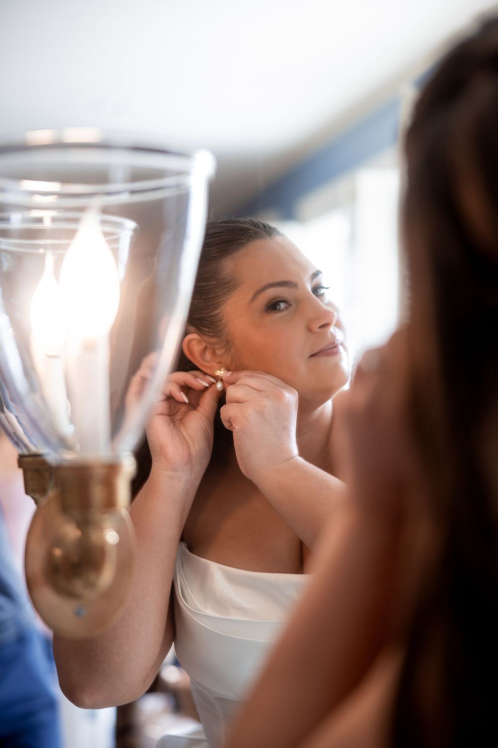 A close-up shot of final wedding preparations with earrings being put on in front of an ornate mirror.