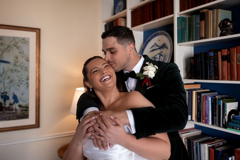 A couple shares intimate moments in a library setting with bookshelves in the background.