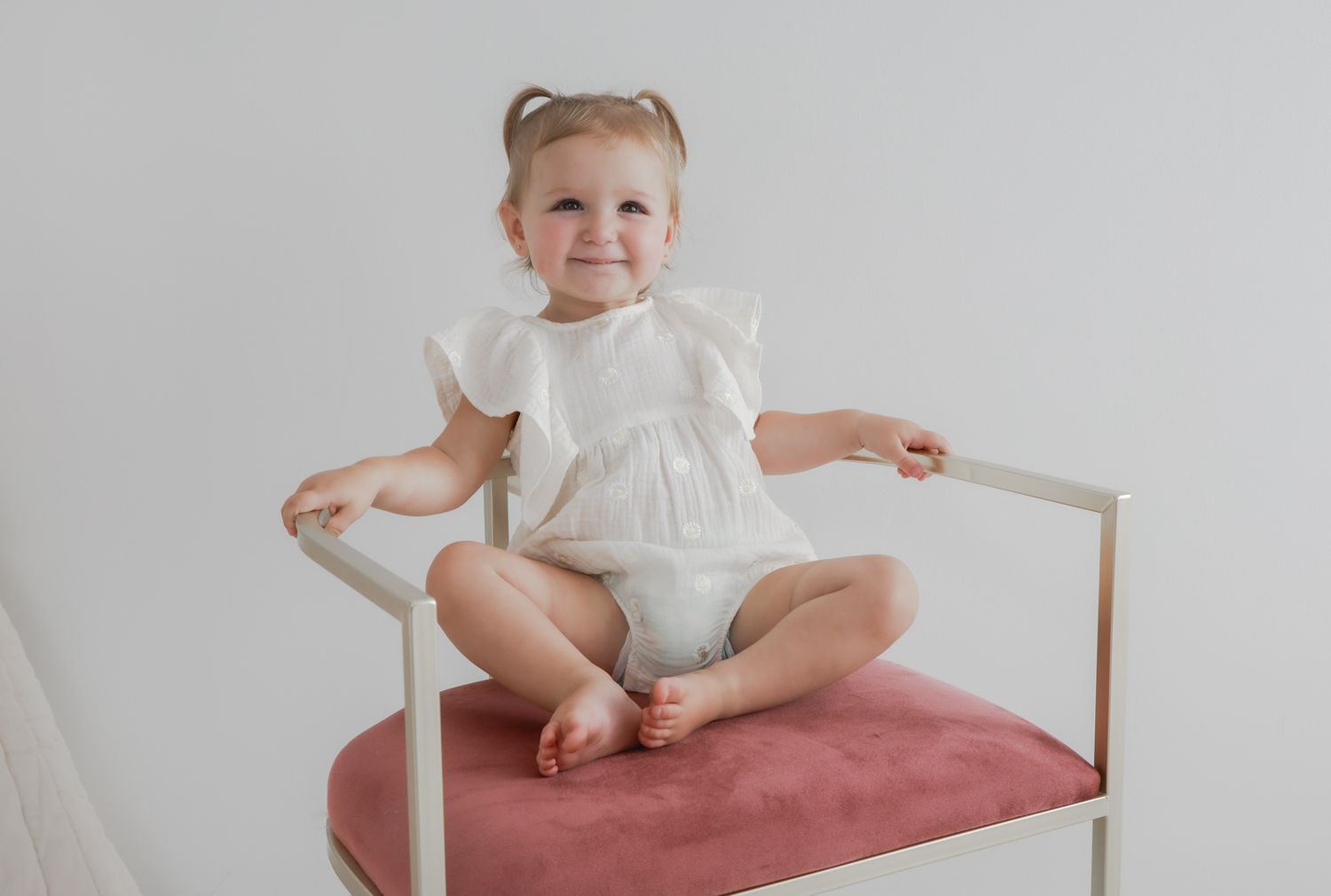 Baby in white dress sits on red cushioned chair showing different playful poses in four sequential photos.