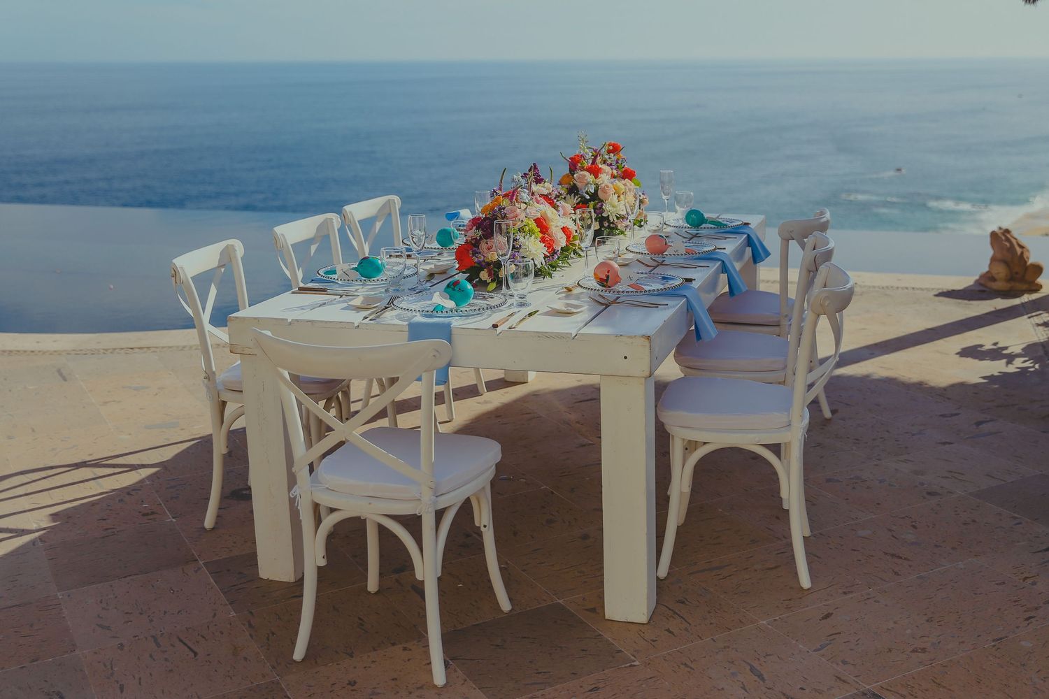 White outdoor dining tables and chairs set up along a beachfront restaurant with ocean views at sunset.Pedregal Los Cabos Wedding Photo
