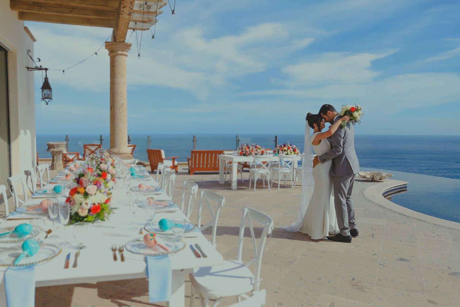 Panoramic view of a beachfront wedding setup with white chairs and decorations overlooking the ocean on a sunny day.