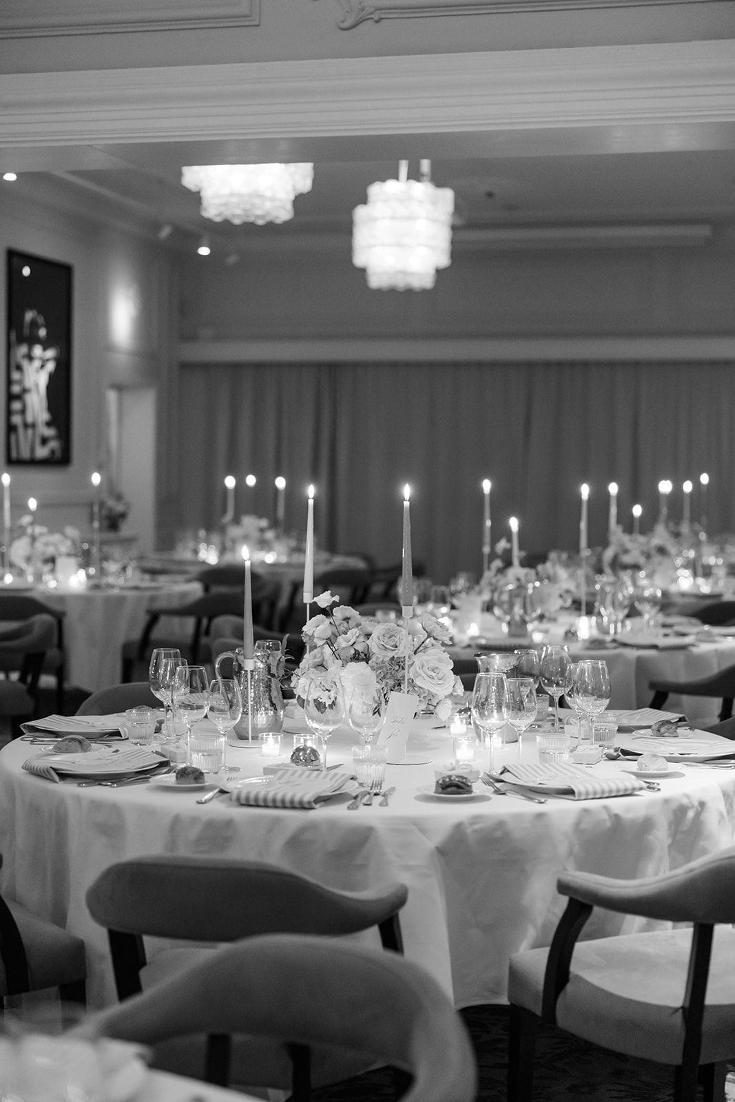 Elegant banquet tables set with white linens, crystal glassware and candlesticks in a formal dining room.