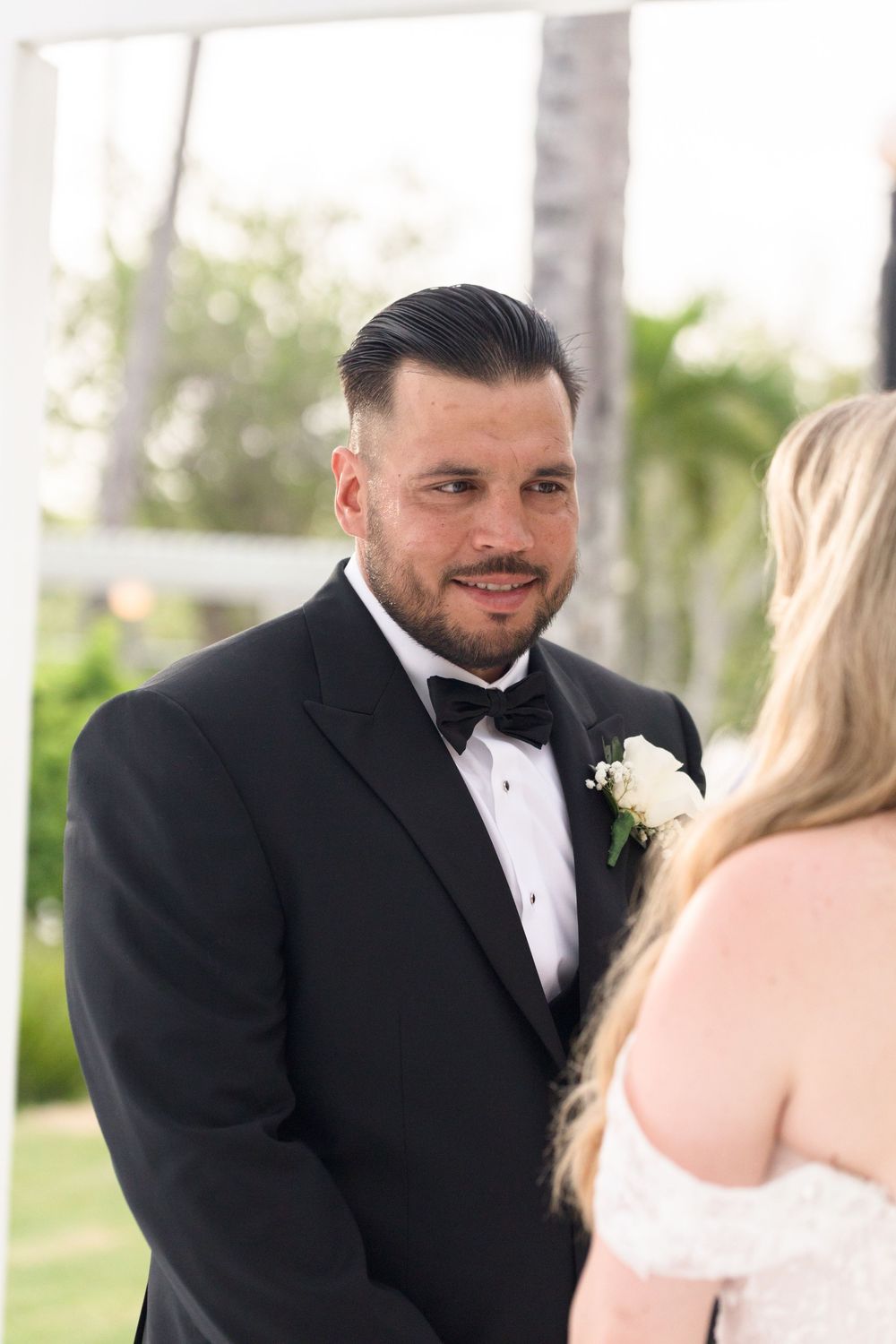 A wedding ceremony moment captured under a white gazebo with lush greenery.