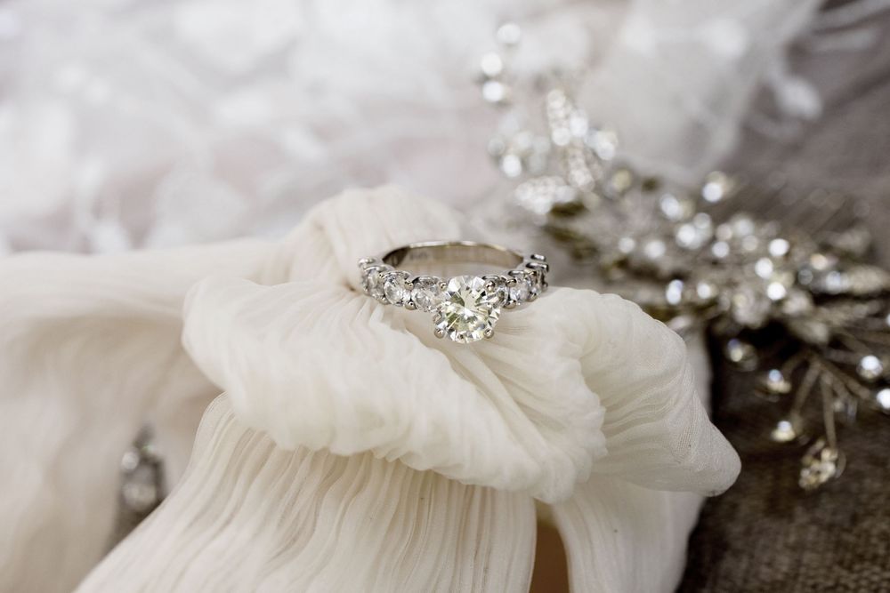 A sparkling diamond engagement ring rests on delicate white fabric alongside crystal embellished accessories.