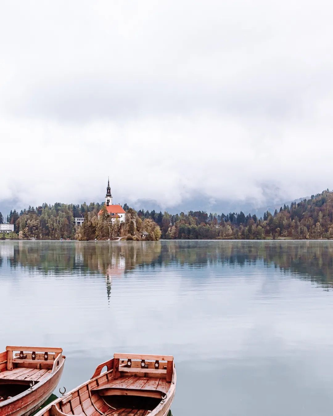 Wooden rowing boats on the shore with Lake Bled church in the distance.