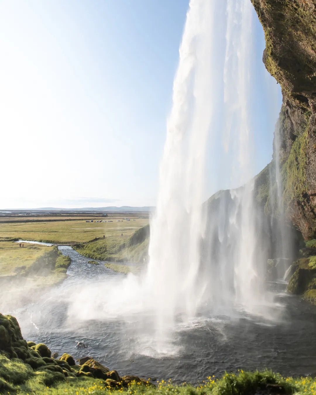 Tall Icelandic waterfall cascading in bright sunlight over green cliffs.