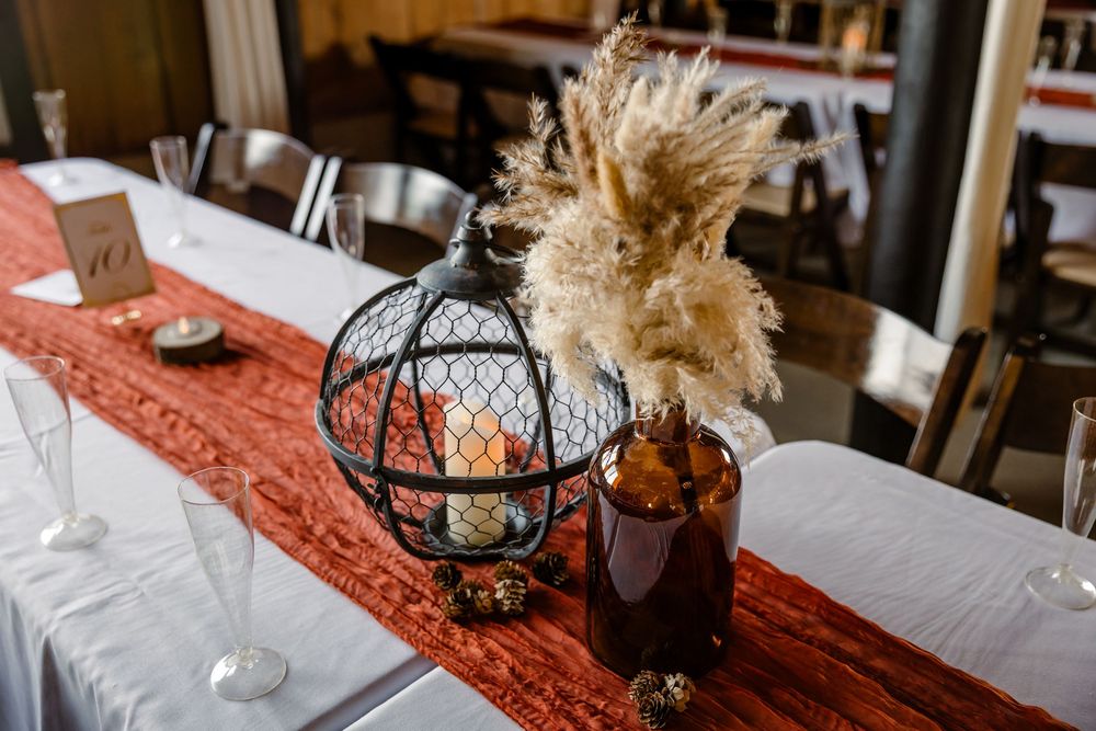 Rustic fall wedding reception decor with lanterns, pampas grass, and orange table runners creating a warm atmosphere.