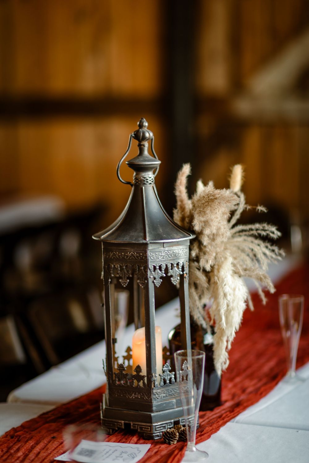 Decorative metal lantern with candle light and pampas grass on table setting for rustic wedding reception.