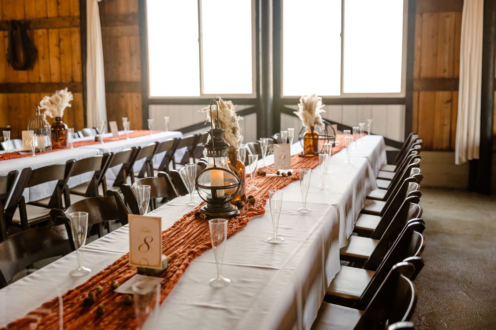 Long banquet tables with white linens and red runners set up in rustic wooden barn venue.