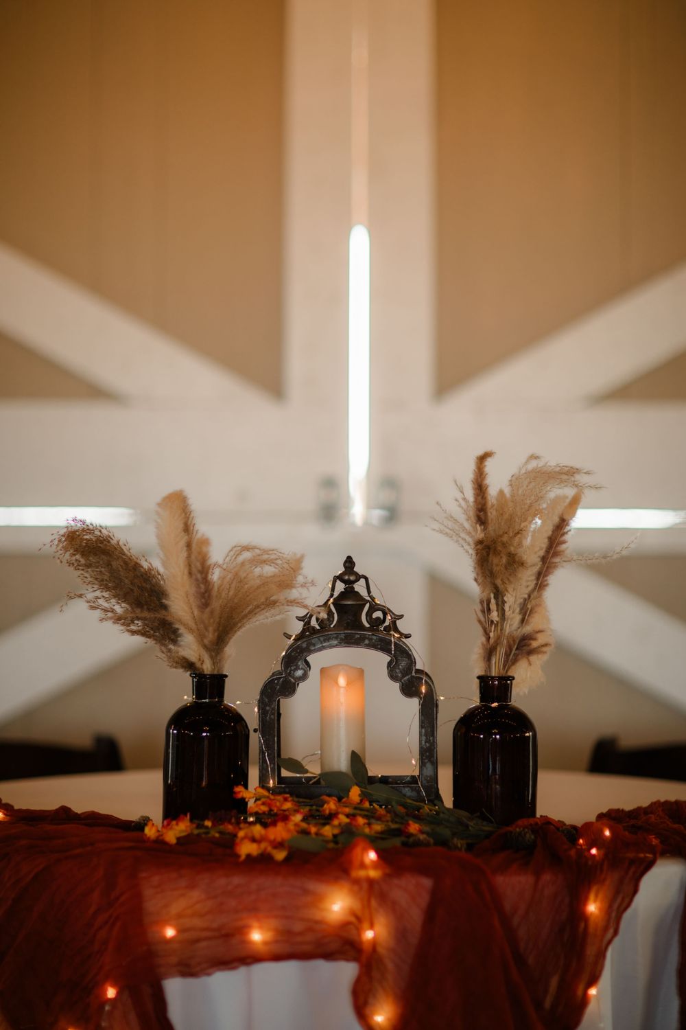 Decorative lanterns with pampas grass and string lights create a cozy autumn ambiance against white walls.