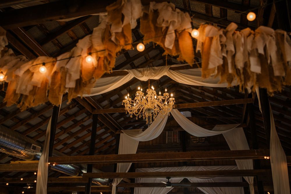 Rustic barn interior decorated with draped fabric, chandeliers, and warm lighting for an elegant wedding reception.