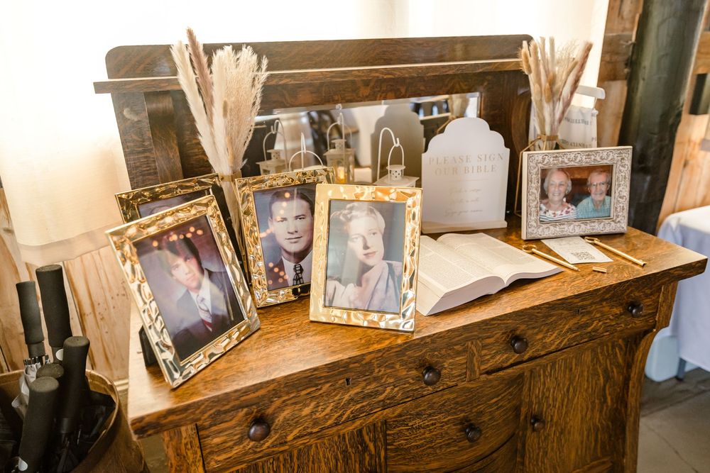 A wooden shelf displaying multiple framed family photographs arranged in a decorative manner against a beige wall.