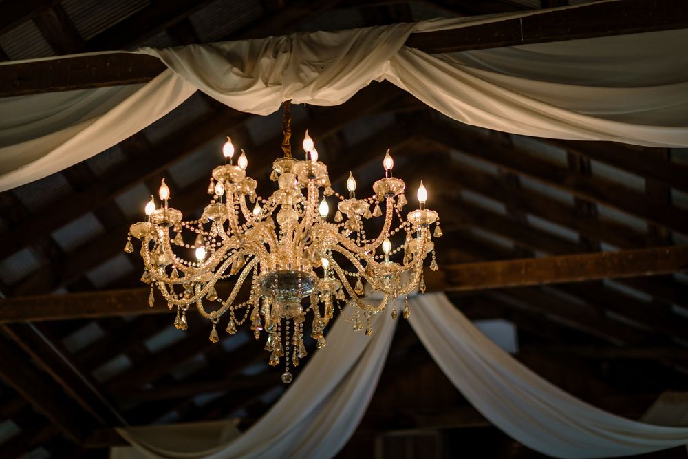 Elegant crystal chandeliers hang from a white draped ceiling creating romantic wedding reception lighting.