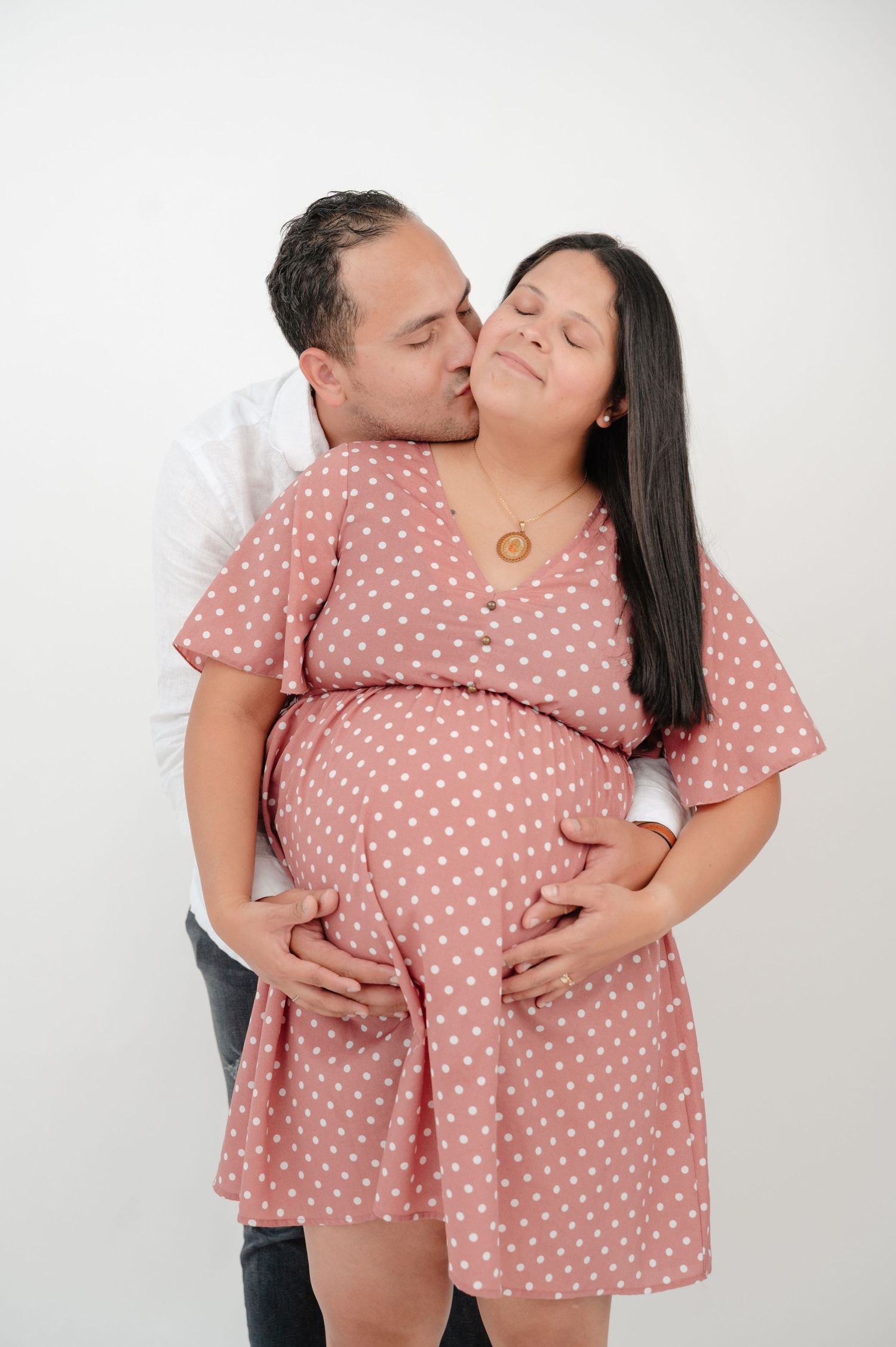 A couple shares a tender moment in matching pink polka dot outfits during a maternity photoshoot.