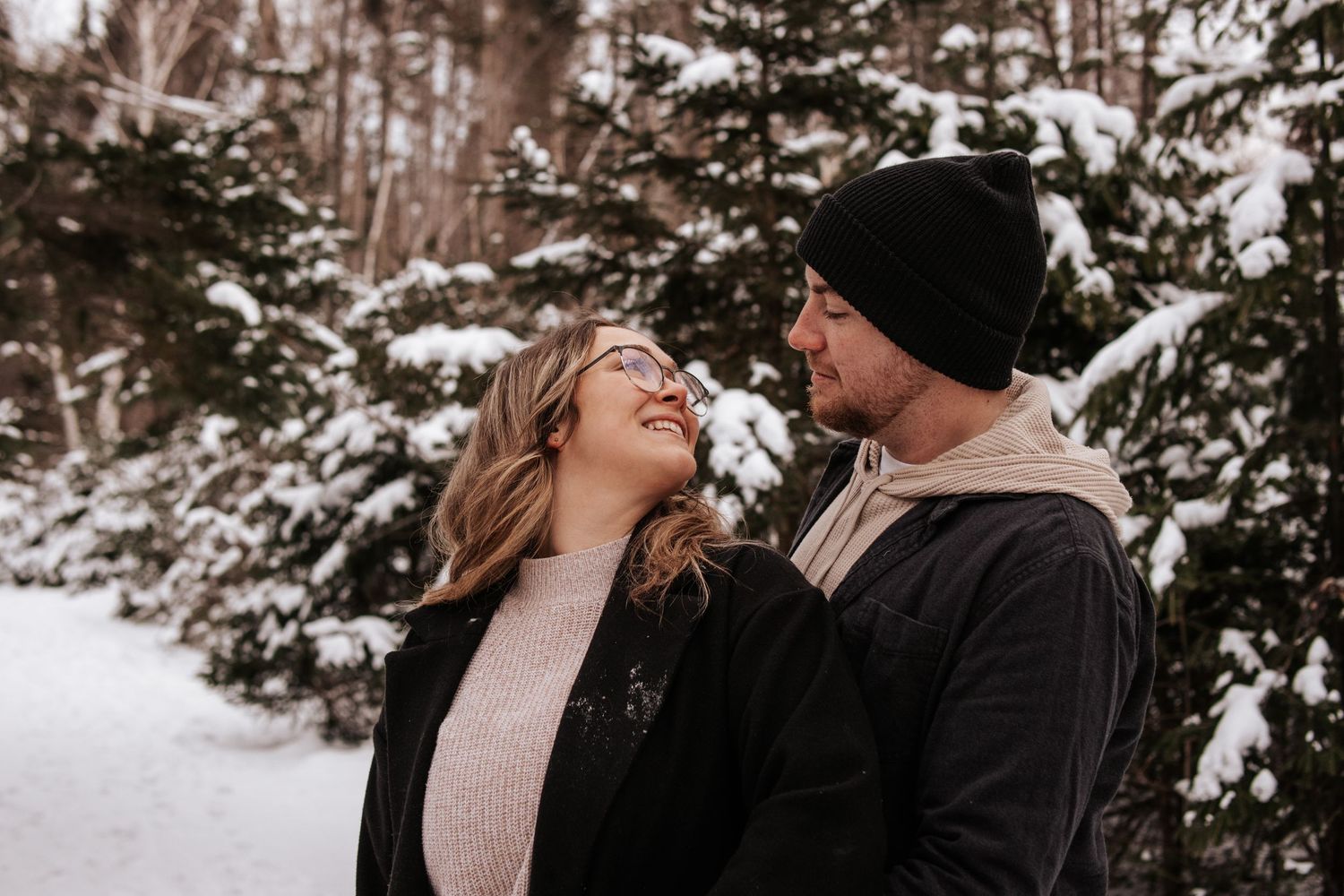 A couple shares an intimate moment together in a snowy winter forest setting.