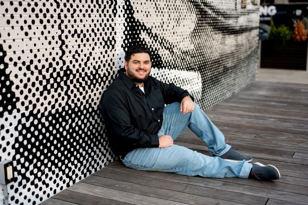 Young man in black shirt sitting casually on wooden deck against black and white mural.
