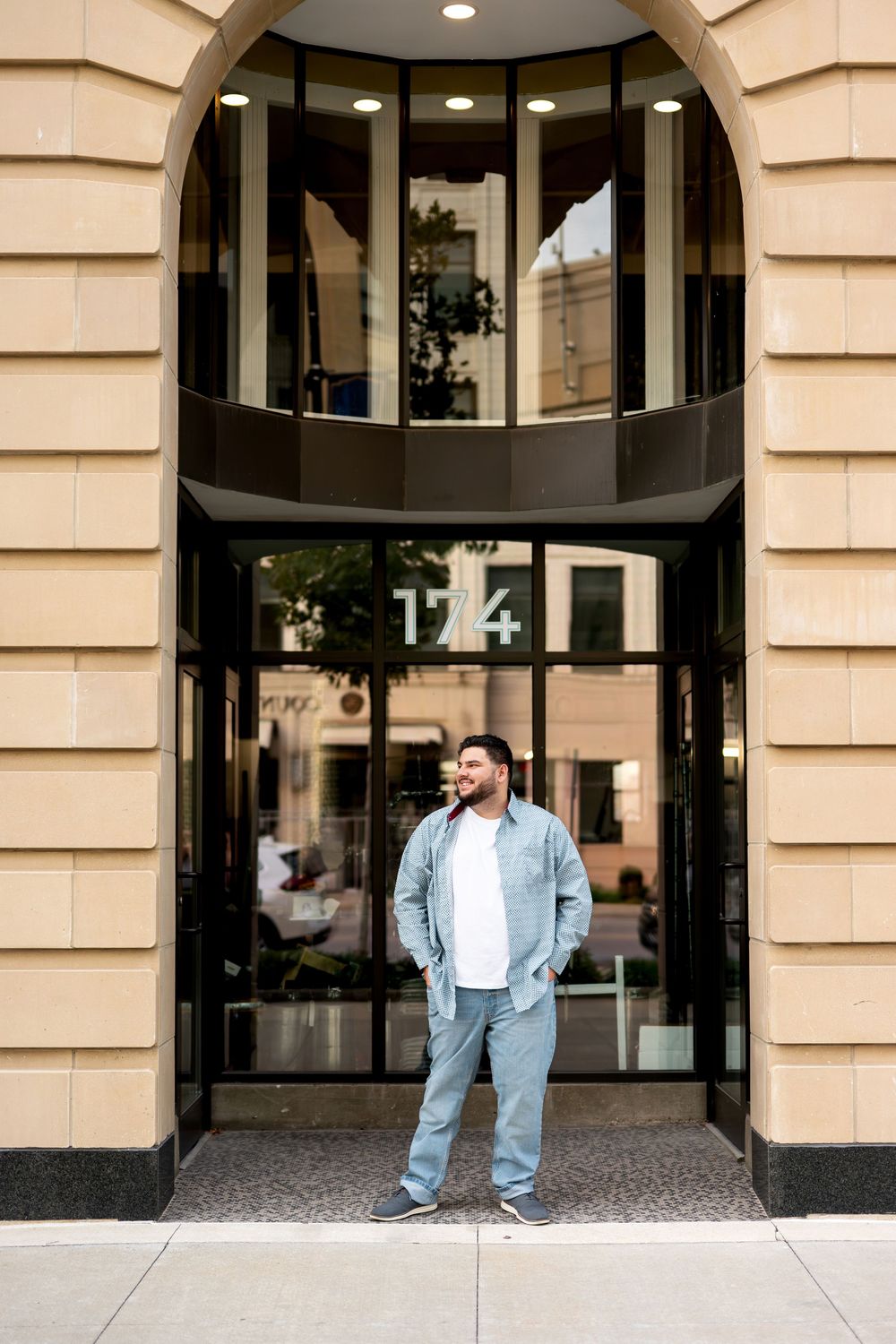 Bearded young man in blue outfit standing relaxed outside arched entrance of building 174.