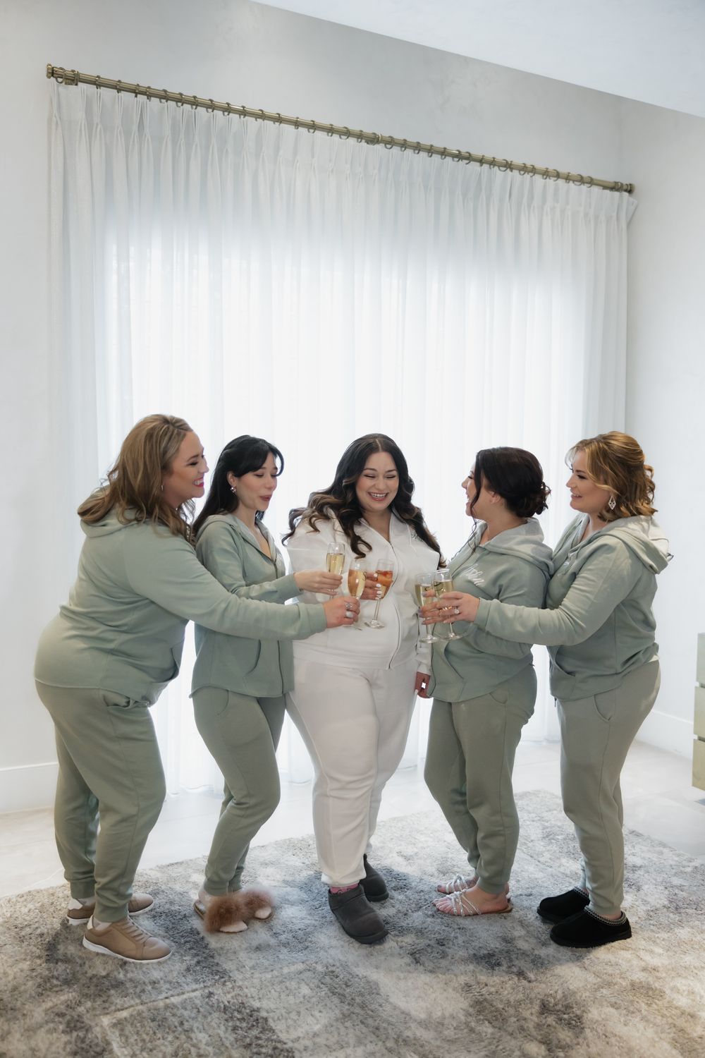 Wedding party wearing matching sage green outfits posing playfully in a bright white room.