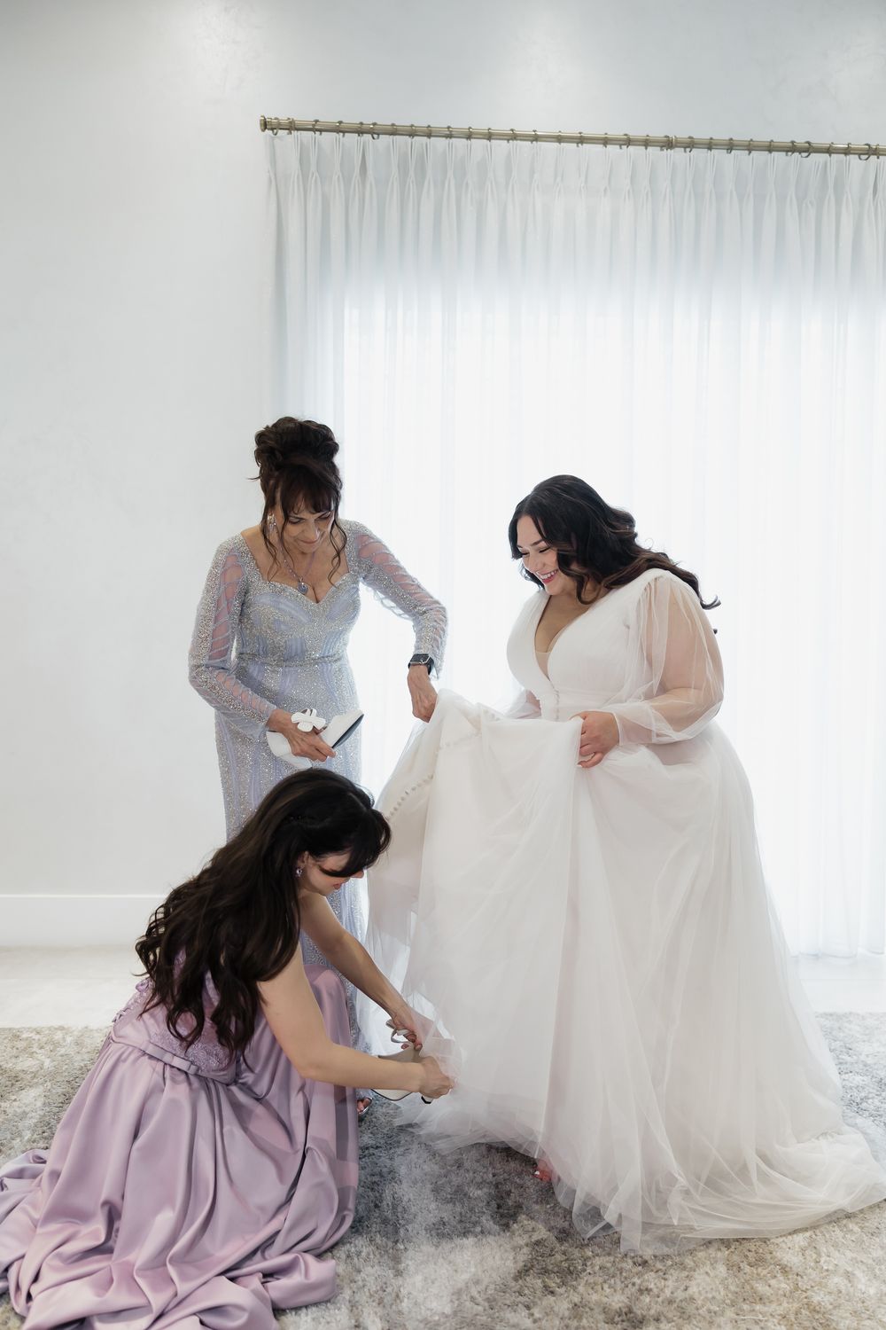 Wedding party helping with dress preparations in a bright white studio setting.