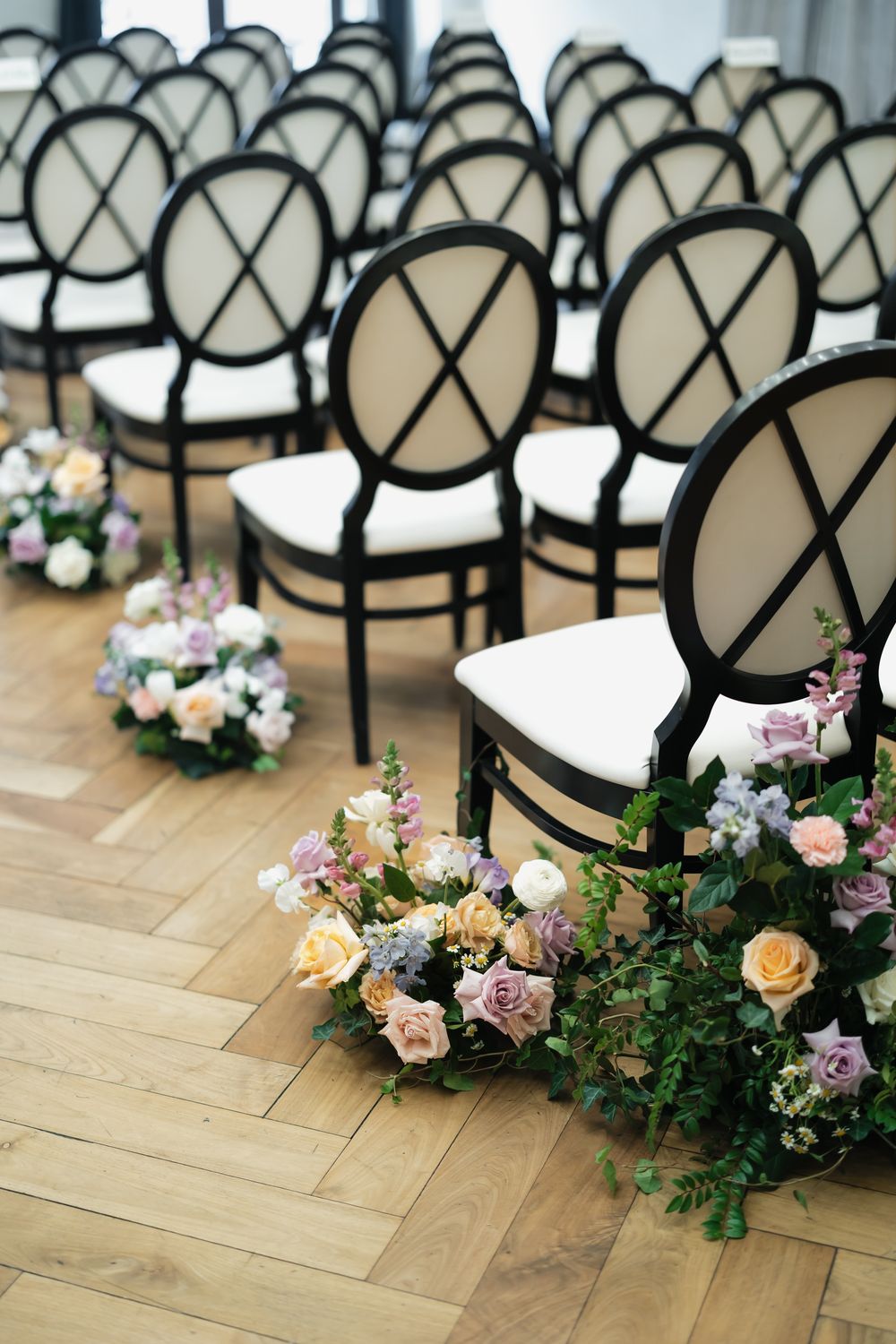 Modern black and white chairs lined up with delicate floral aisle decorations.