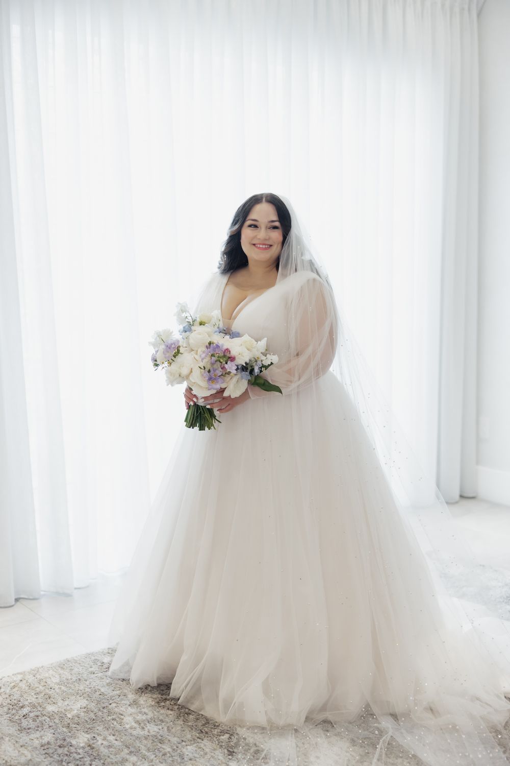 Elegant bridal portraits in a flowing white wedding gown against white curtains.