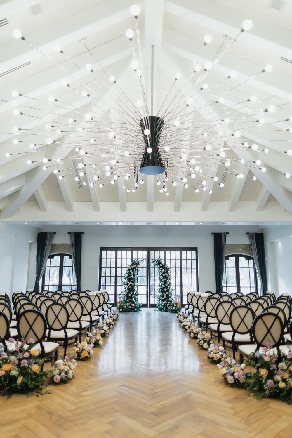 Elegant wedding venue with string lights and herringbone flooring decorated with floral arrangements.