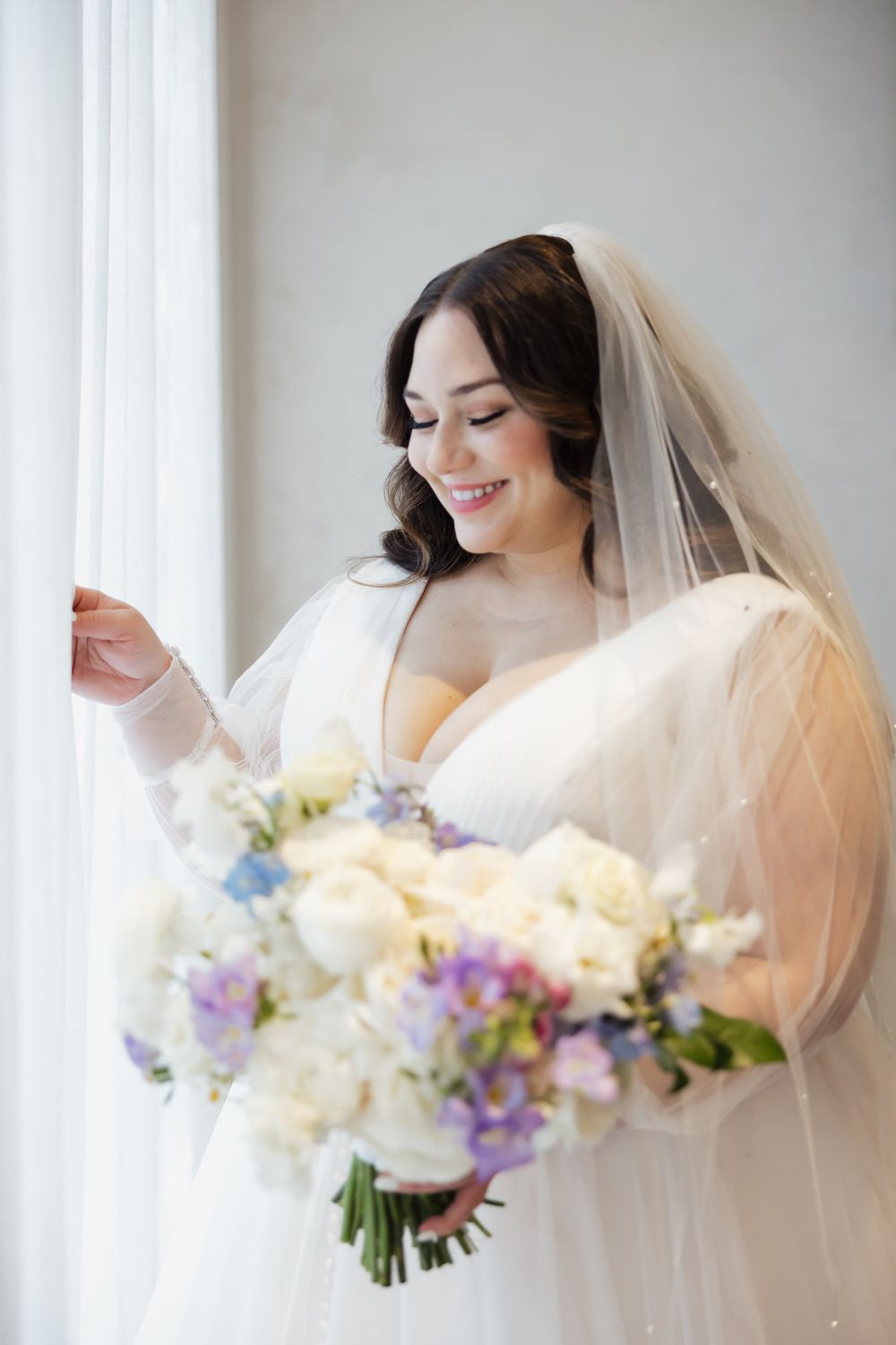 Bride holding a romantic pastel bouquet with purple and white flowers against a light background.