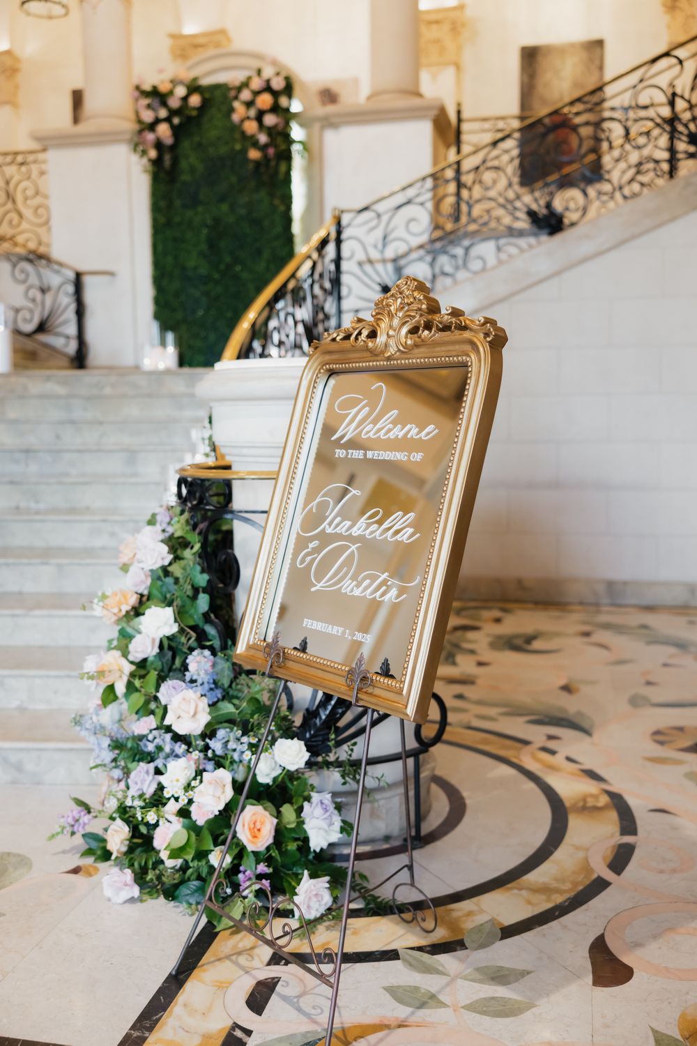 Gold-framed welcome signs with elegant calligraphy and floral arrangements on marble steps.