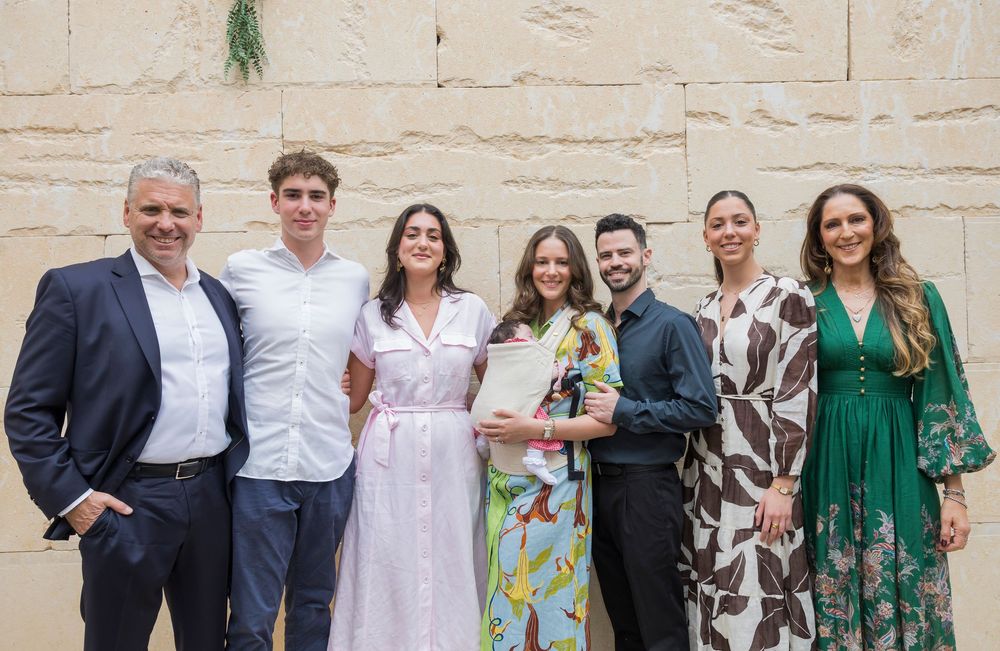 A group of people standing together against a beige stone wall backdrop.