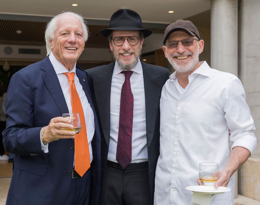 A group of men in business attire and casual clothing smile together at an outdoor event.