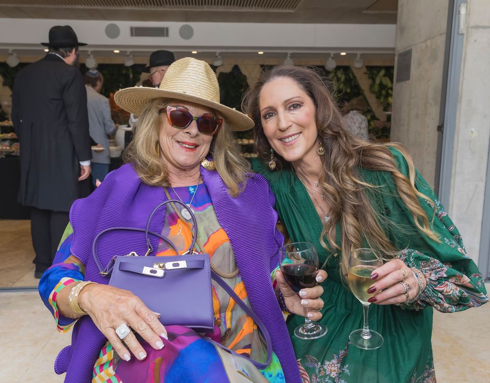 Two people in colorful outfits smile and pose together at what appears to be a social gathering or event.