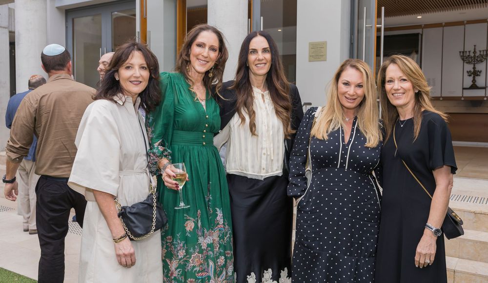 A group of people gathered at a social event wearing elegant cocktail attire in emerald green and navy blue dresses.